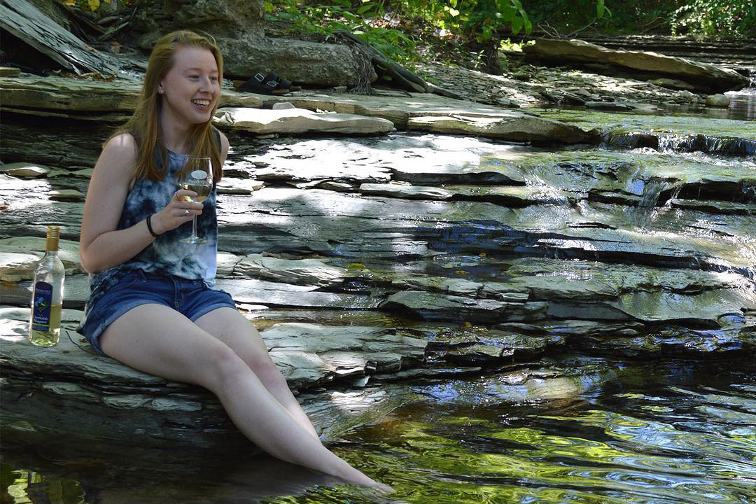 A women enjoying wine sitting on rocks by a creek at Presque Isle wine Cellars