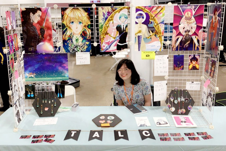 A person sitting at a table at vendor stall with Geek wallposters