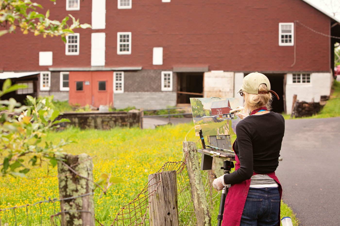 A woman live painting a barn in front